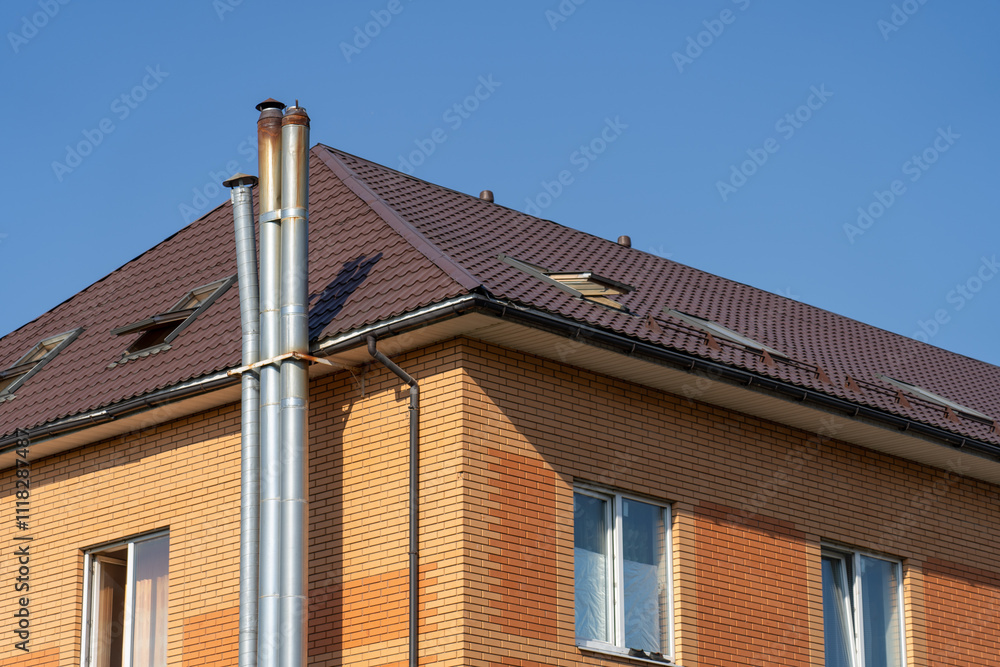 A two-story residential building features a brick facade, sloped roof, and silver chimneys, set against a bright blue sky on a sunny day A two-story residential building features a brick facade, sloped roof, and silver chimneys, set against a bright blue sky on a sunny day