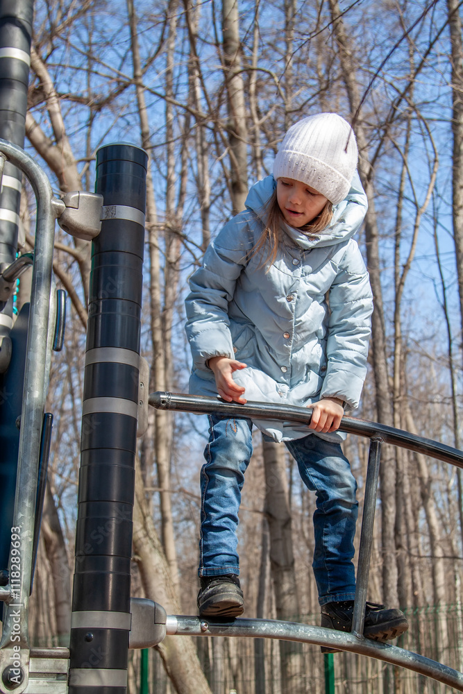 A young girl explores playground equipment surrounded by trees under a clear blue sky on a sunny day in early spring A young girl explores playground equipment surrounded by trees under a clear blue sky on a sunny day in early spring