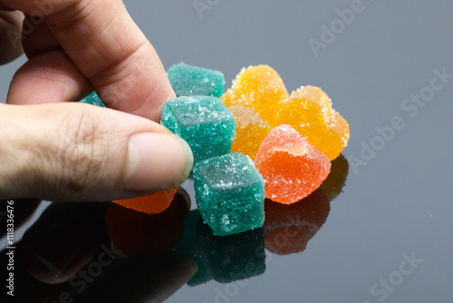 Close-Up of Hand Picking Colorful Sugary Jelly Candy Cubes on Black Surface