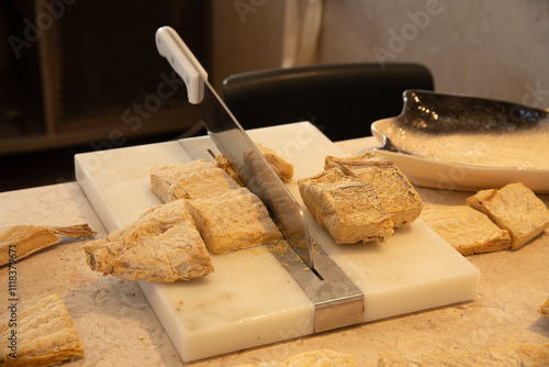 Knife Cutting Dry Fish on White Board with Black Bowl in Background photo