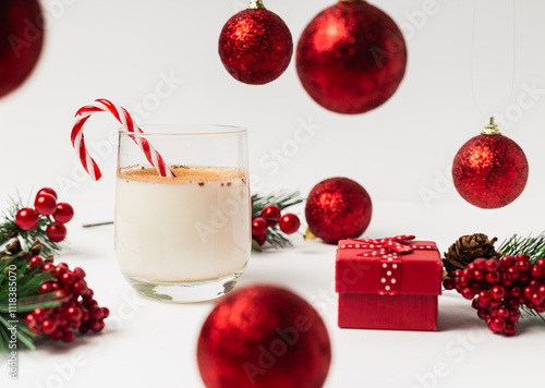 Glass of eggnog with pine needles, one small present box and christmas balls on a white background