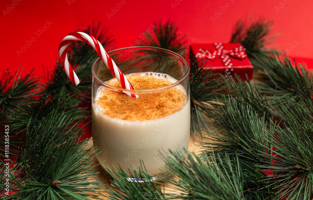 Glass of eggnog with pine needles, one small present box on a red background Glass of eggnog with pine needles, one small present box on a red background