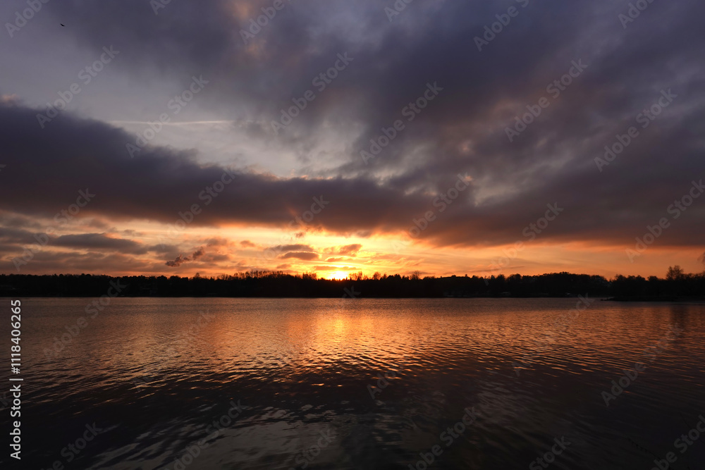 Beautiful natural autumn landscape with dramatic sunset and forest silhouette on horizon against calm river Beautiful natural autumn landscape with dramatic sunset and forest silhouette on horizon against calm river