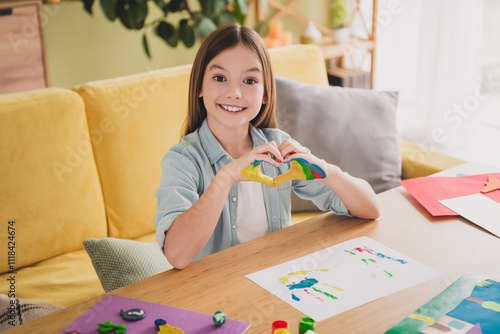 Smiling young girl holding colorful clay heart at home in a cozy living room, embracing creativity and happiness