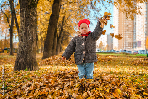 Caucasian cute little child girl toddler is playing with a bunch of autumn leaves in the park on a golden autumn sunny day.