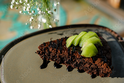 chocolate brownie served with fresh kiwi slices, on trend contemporary ceramic clay plate on sunny day in cafe