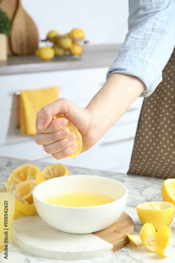Woman squeezing lemon juice into bowl at marble table, closeup