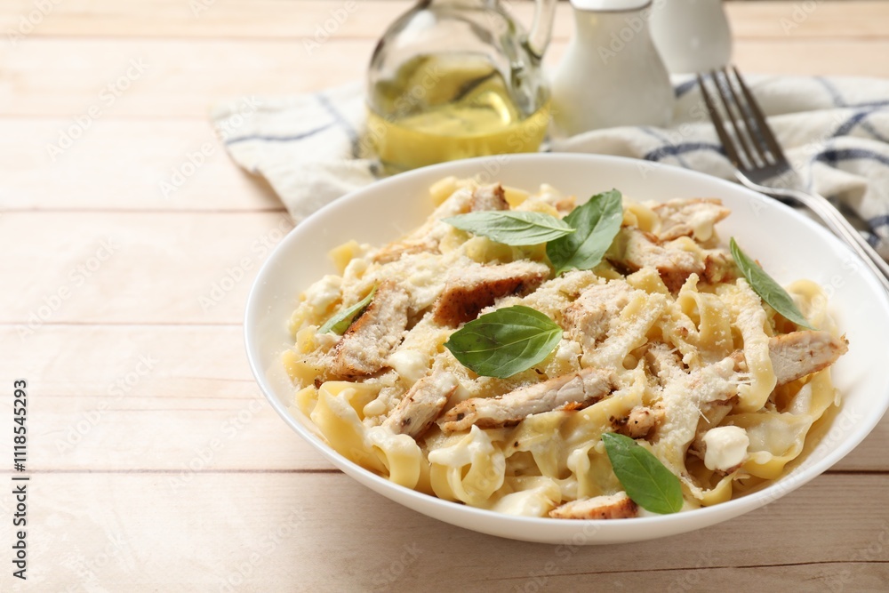 Tasty Alfredo pasta with chicken on light wooden table, space for text Tasty Alfredo pasta with chicken on light wooden table, space for text