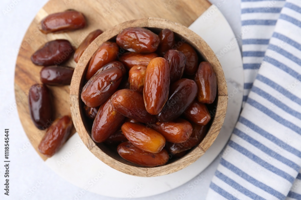 Tasty dried dates in wooden bowl on white table, top view Tasty dried dates in wooden bowl on white table, top view