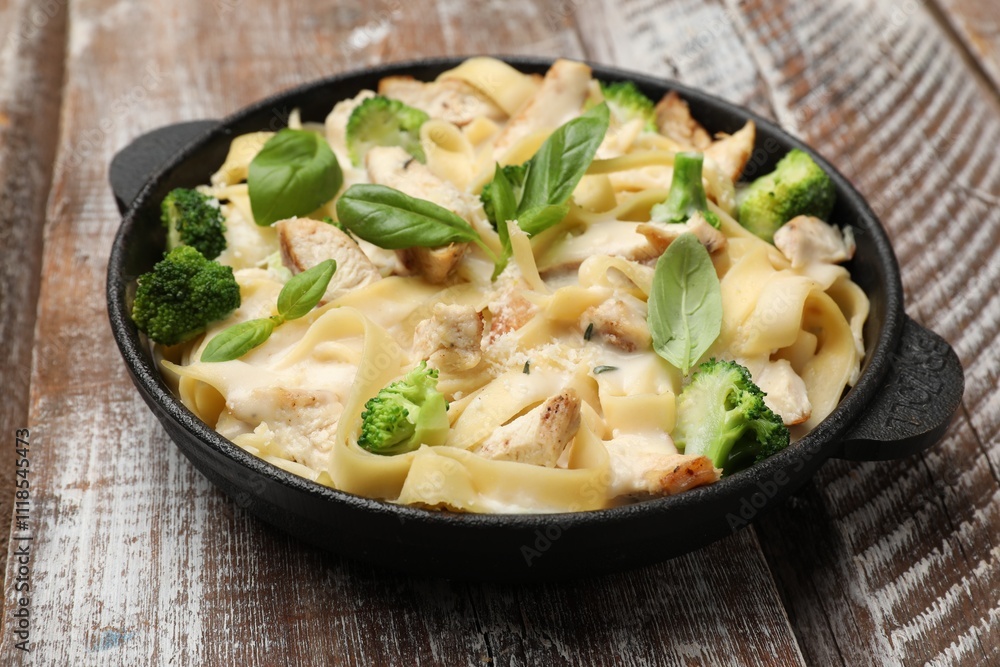 Delicious pasta Alfredo with chicken, cheese, creamy sauce, broccoli and basil on wooden table, closeup Delicious pasta Alfredo with chicken, cheese, creamy sauce, broccoli and basil on wooden table, closeup