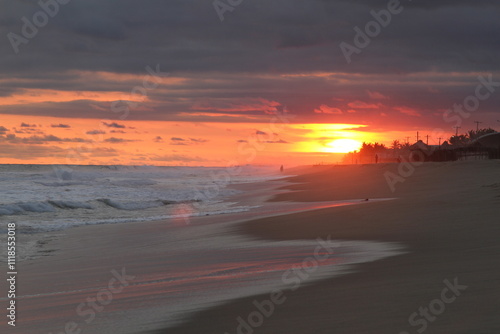 Beautiful sunset on the beach, a cloudy sky with orange tones and a few people in the distance.