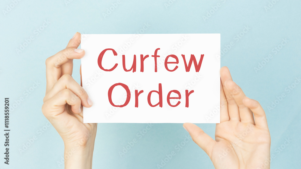 CURFEW ORDER text words inscription on white paper in male hand on white background CURFEW ORDER text words inscription on white paper in male hand on white background