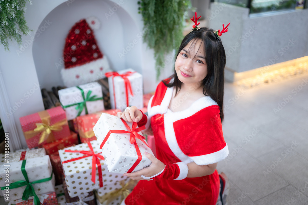 Portrait Cute Smiling asian girl in red santa with looking to the camera near Christmas greeting picture parcel decoration on Christmas tree background Decoration During Christmas and New Year.