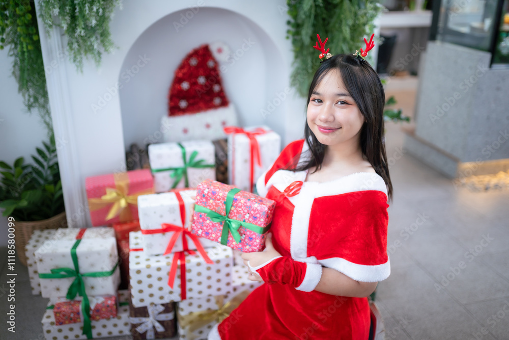 Portrait Cute Smiling asian girl in red santa with looking to the camera near Christmas greeting picture parcel decoration on Christmas tree background Decoration During Christmas and New Year. Portrait Cute Smiling asian girl in red santa with looking to the camera near Christmas greeting picture parcel decoration on Christmas tree background Decoration During Christmas and New Year.