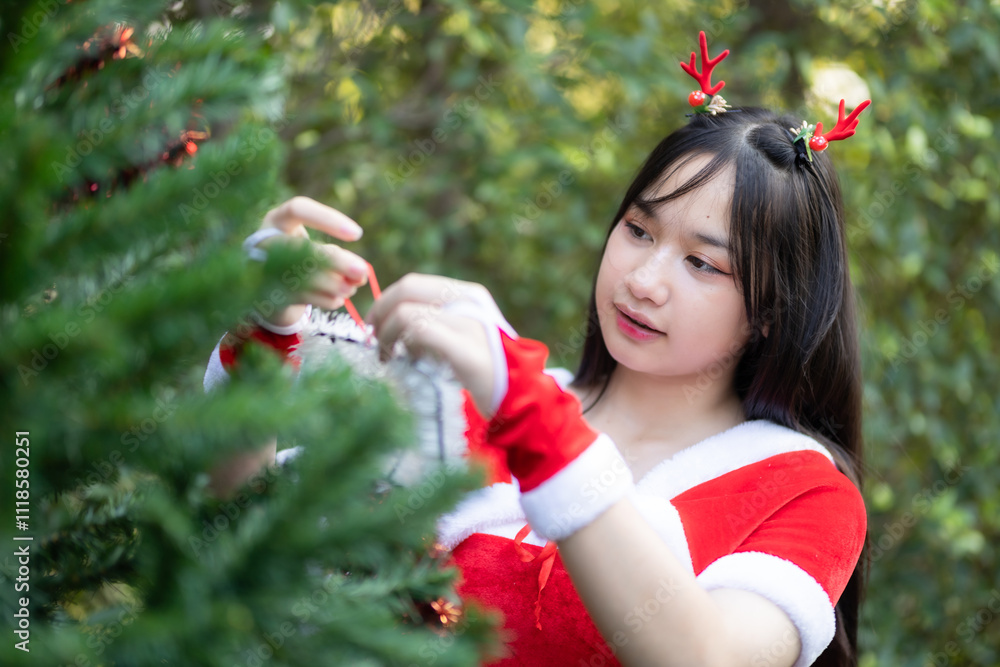 Portrait Cute Smiling asian girl in red santa with looking to the camera near Christmas greeting picture parcel decoration on Christmas tree background Decoration During Christmas and New Year.