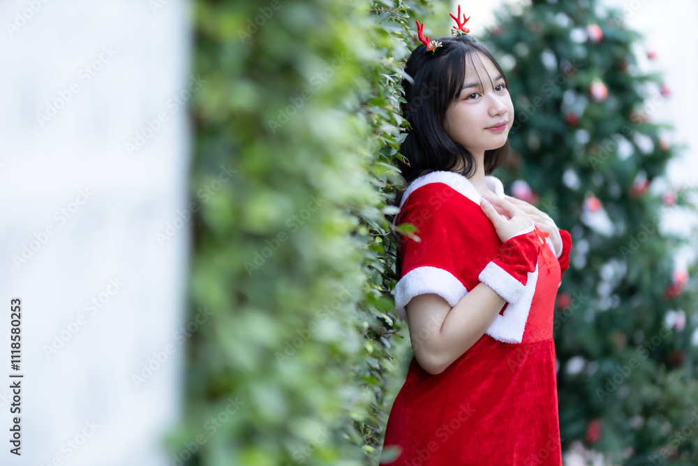 Portrait Cute Smiling asian girl in red santa with looking to the camera near Christmas greeting picture parcel decoration on Christmas tree background Decoration During Christmas and New Year.