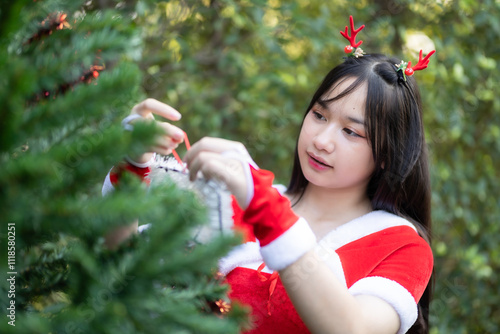 Obraz na płótnie Portrait Cute Smiling asian girl in red santa with looking to the camera near Christmas greeting picture parcel decoration on Christmas tree background Decoration During Christmas and New Year. w salonie