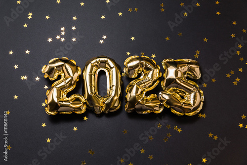 New year 2025 balloon celebration card. Gold foil helium balloon number 2025, party decoration, gold confetti stars on black background. Copy space, flat lay, merry christmas, happy holidays concept.