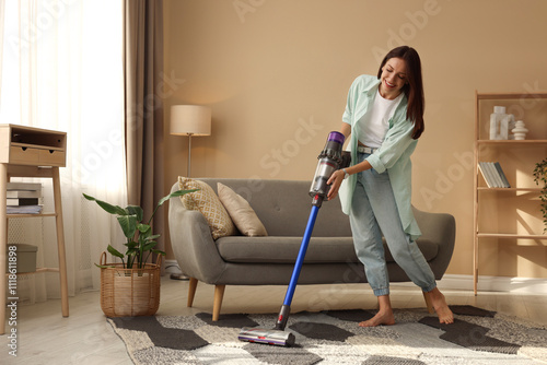 Billede på lærred Smiling young woman cleaning rug with cordless vacuum cleaner in living room