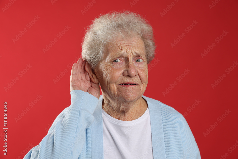 Senior woman showing hand to ear gesture on red background Senior woman showing hand to ear gesture on red background