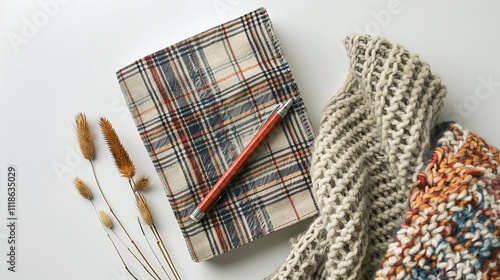 Plaid notebook with pencil resting on soft knitted scarf, dried wheat stems on white background, warm rustic theme, cozy writing inspiration, copy space for notes

 photo