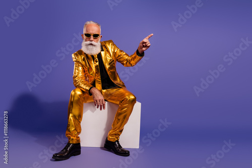 Full size photo of old macho man sit white cube point empty space dressed glamour stylish golden outfit party isolated on purple background