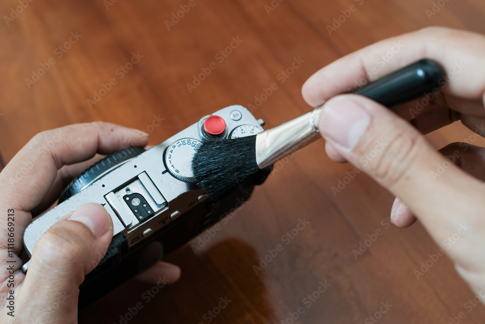 Fototapeta premium Cleaning the camera body with cleaning brush from dust and dirt on wooden table and. Cleaning and care of the camera body. The concept of care for professional photographic equipment.