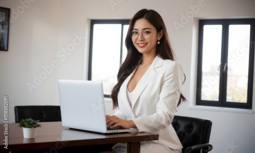 business woman in white suit sitting at table with laptop, smiling confidently in modern office setting. Her glasses add professional touch to her appearance