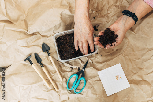 Kraft paper background, fertile soil and garden tools, top view. Hands planting seeds