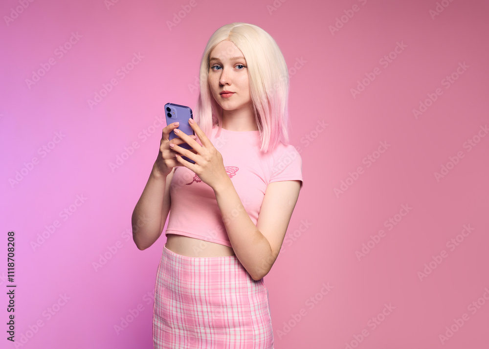 A stylish blonde dressed in fashionable 2yk style clothes poses with a phone in her hands standing on a pink background A stylish blonde dressed in fashionable 2yk style clothes poses with a phone in her hands standing on a pink background
