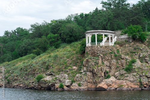 Scenic view of a white gazebo on a rocky cliff by a river, surrounded by lush greenery. Perfect for nature, travel, and architecture themes photo