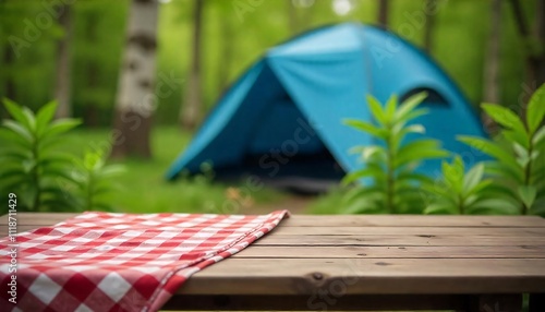 A empty wooden table in the foreground with a tent and trees in the blurred background, suggesting an outdoor camping scene in a forest photo