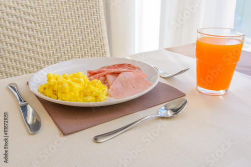 Breakfast including scrambled egg, ham, salami, and orange juice. photo