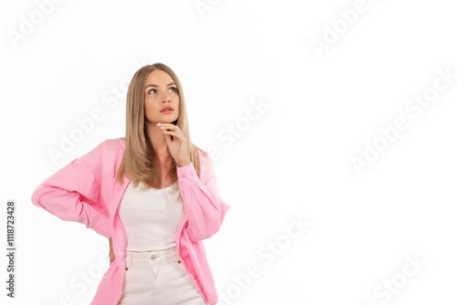 A woman with long hair wearing a pink jacket and white shirt, thinking thoughtfully while standing in a bright setting