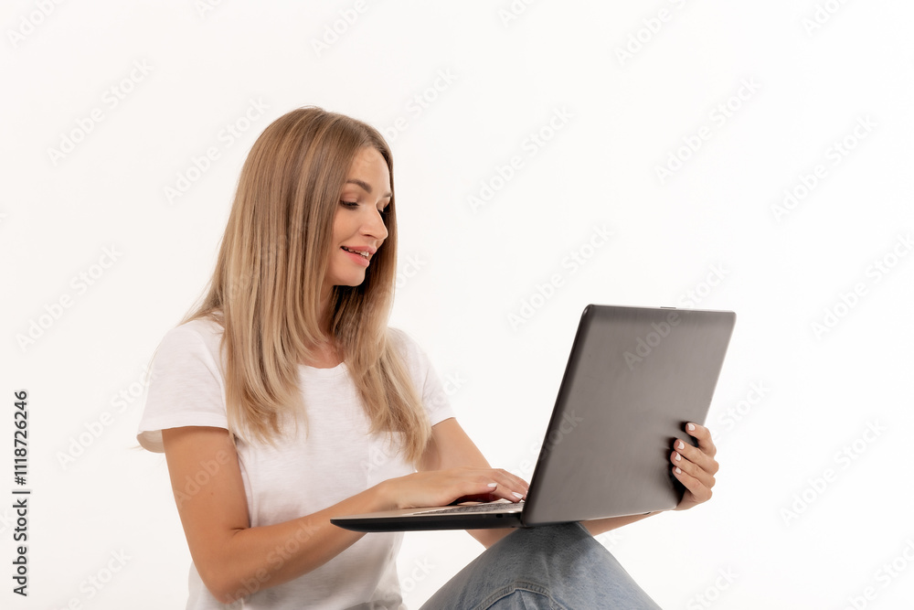 Young woman working on a laptop while sitting casually on a plain background during daytime Young woman working on a laptop while sitting casually on a plain background during daytime