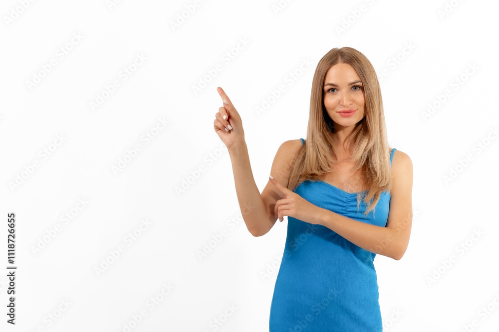 Young woman in a blue dress pointing upward against a white background, showcasing enthusiasm and engagement Young woman in a blue dress pointing upward against a white background, showcasing enthusiasm and engagement