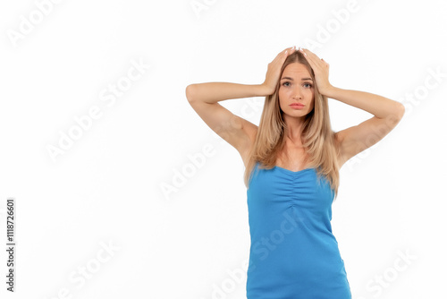 A young woman expresses frustration while standing against a white background in a casual blue tank top