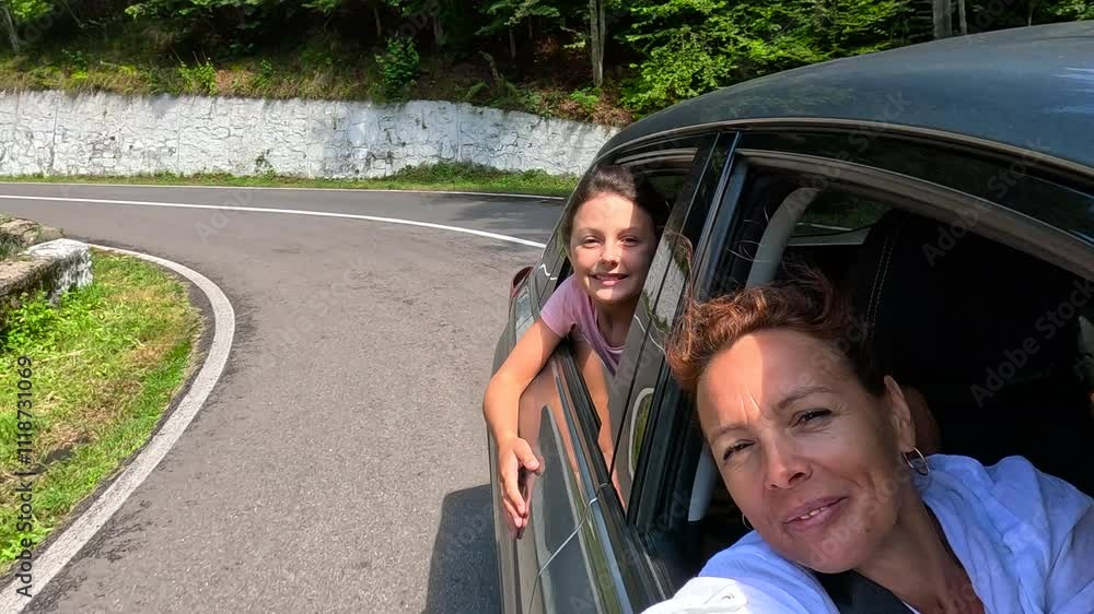 Happy family car trip. Woman and her daughter enjoy a fun road trip, taking selfies while driving along a scenic mountain road. Laughter and joy fill the car as they create lasting memories together