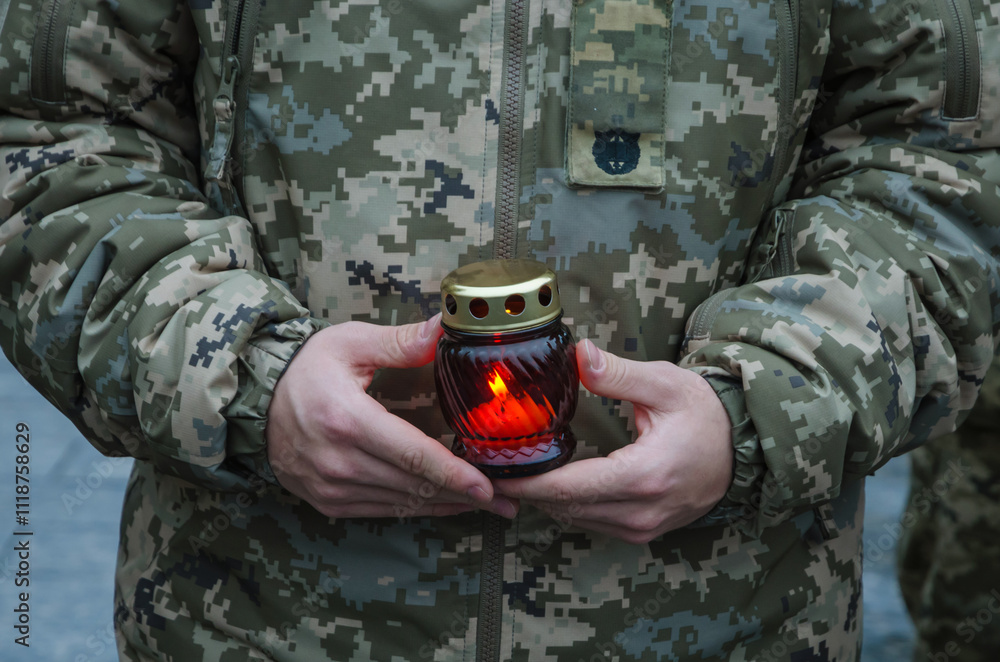 A Ukrainian soldier in military uniform holds a memorial lamp in his hands. A soldier holds a candle in his hands. Honoring the memory of the military.