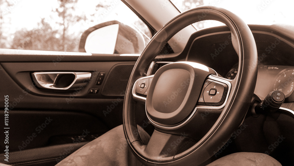 Obraz premium Black leather car steering wheel with a view of the road through the windshield. Colour of the year Mocha Mousse.