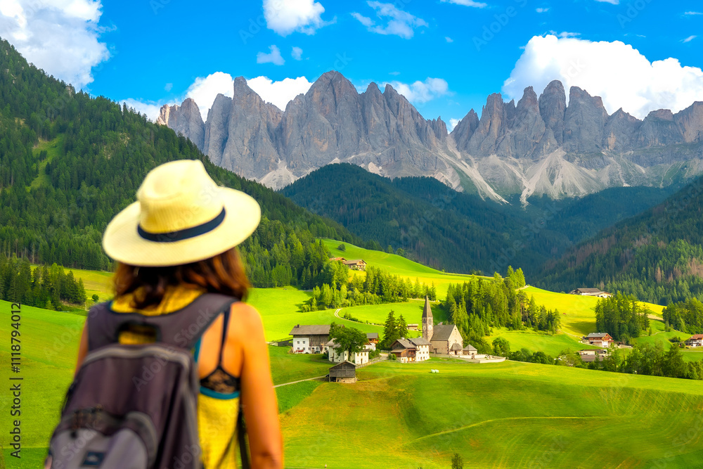 Naklejka premium Tourist hiking in the dolomites admiring the funes valley and st. Magdalena church