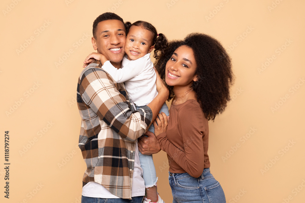 Happy family. Cheerful black parents holding their little daughter on hands, embracing and posing together over beige studio background, smiling at camera