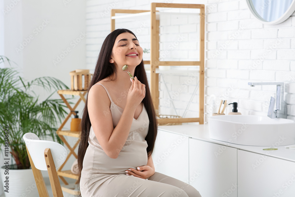 Young pregnant woman using facial massage tool in bathroom Young pregnant woman using facial massage tool in bathroom