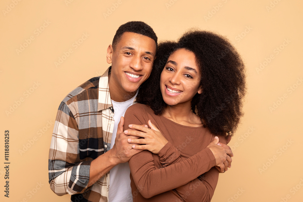 Smiling loving African American man hugging woman, enjoy romantic and closeness, smiling at camera together over beige studio background Smiling loving African American man hugging woman, enjoy romantic and closeness, smiling at camera together over beige studio background