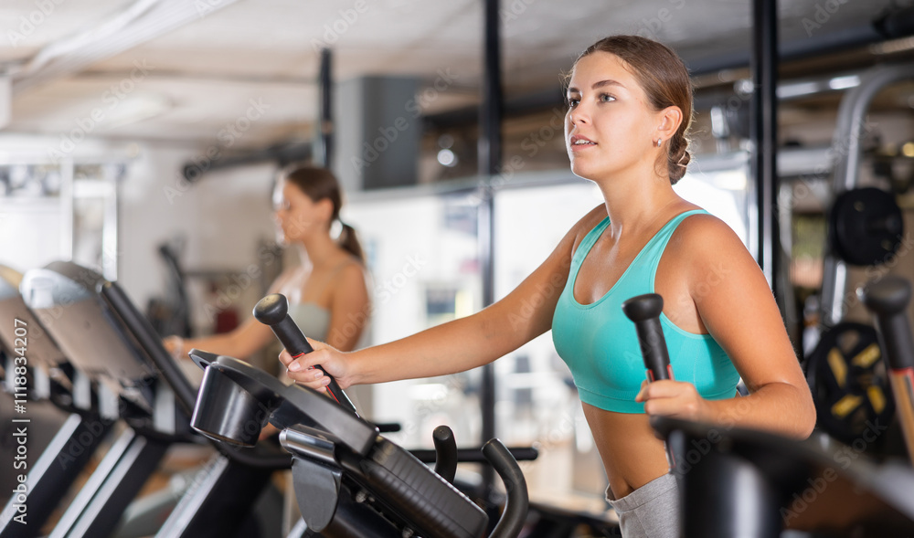 Young sporty girl working out on elliptical machine in gym. Healthy active lifestyle concept Young sporty girl working out on elliptical machine in gym. Healthy active lifestyle concept