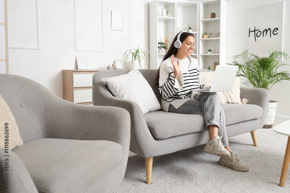 Beautiful young woman in headphones with laptop video chatting on sofa at home Beautiful young woman in headphones with laptop video chatting on sofa at home