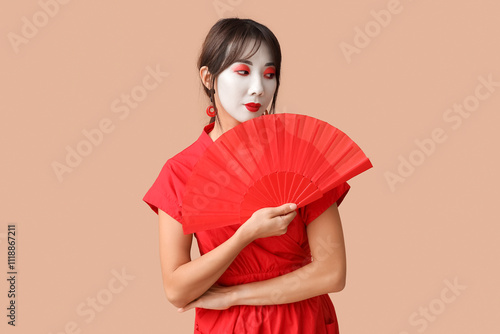 Beautiful young geisha in traditional clothes with fan on beige background photo