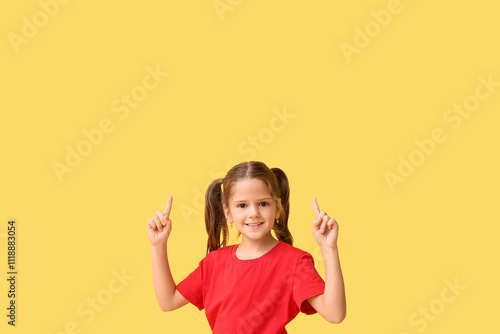 Happy little girl pointing at something on yellow background