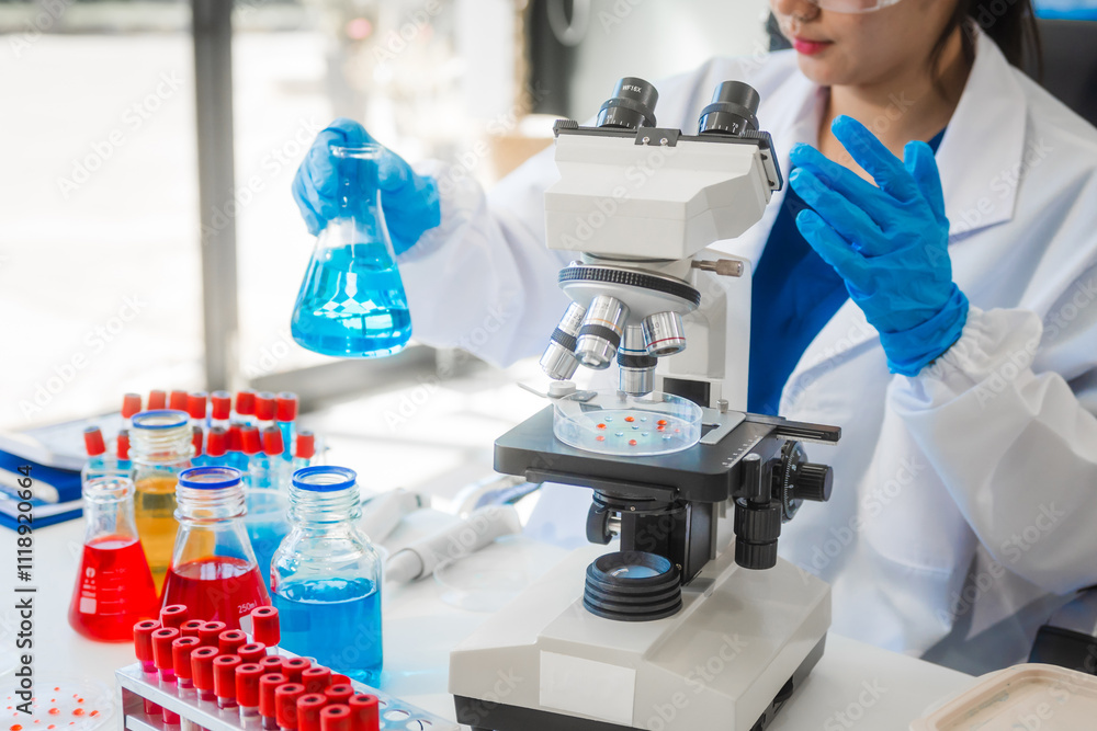 Fototapeta premium A young Asian woman works in a laboratory, conducting chemical and blood tests. Wearing goggles, research and analysis, combining science and technology in a professional and medical environment.