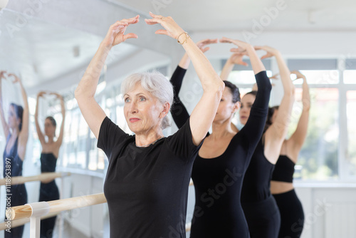 Female ballet dancers doing various ballet movements at a ballet barre in fifth position photo